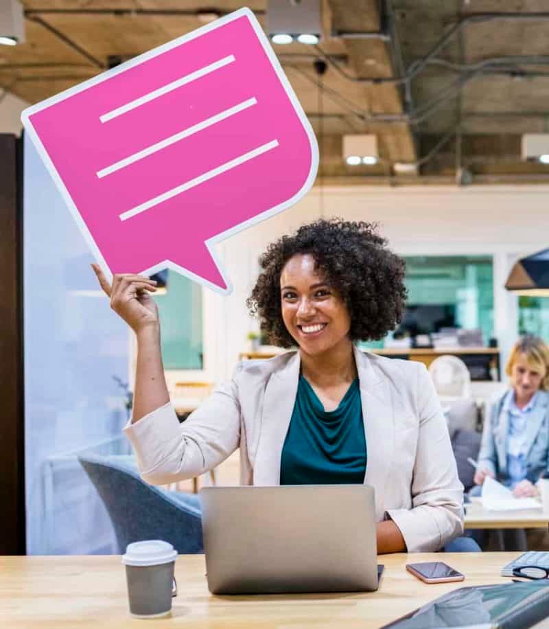 Woman at laptop holding pink chat bubble icon in modern office environment
