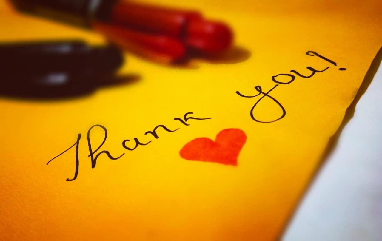 Yellow sticky note reading 'Thank you!' with a red heart, pens in background