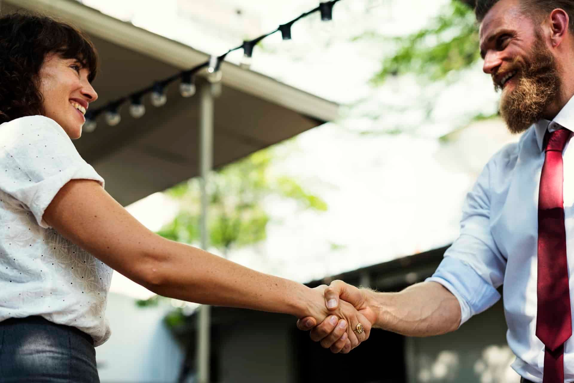 Man and woman shaking hands with warm smiles outside building