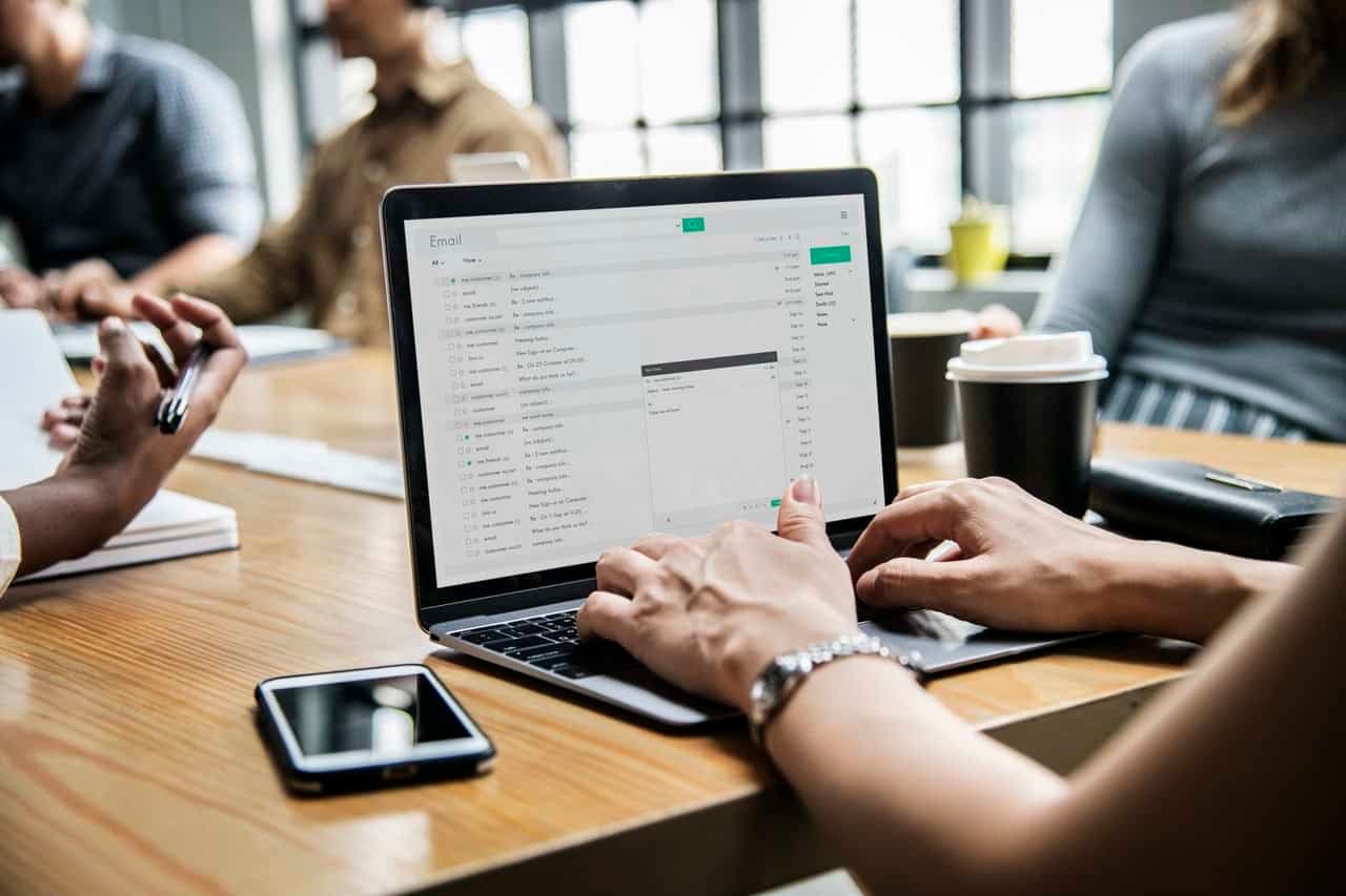 Person checking email on laptop at office desk with coffee cup and smartphone nearby