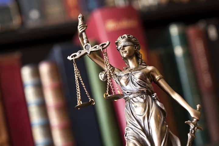 Lady Justice statue holding scales with law books in background