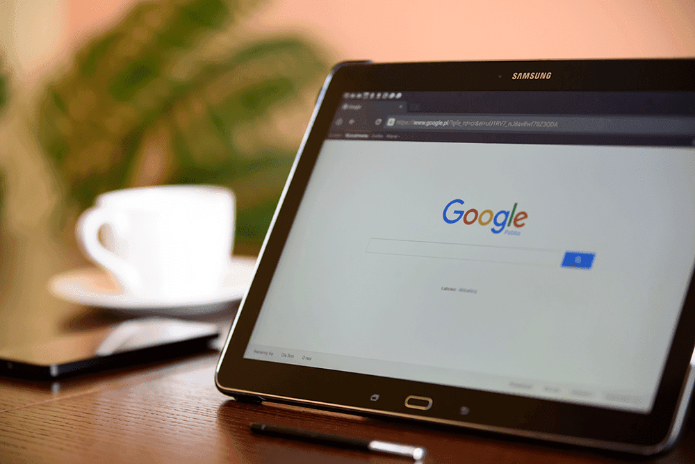 Tablet displaying Google search page with coffee cup and plant background
