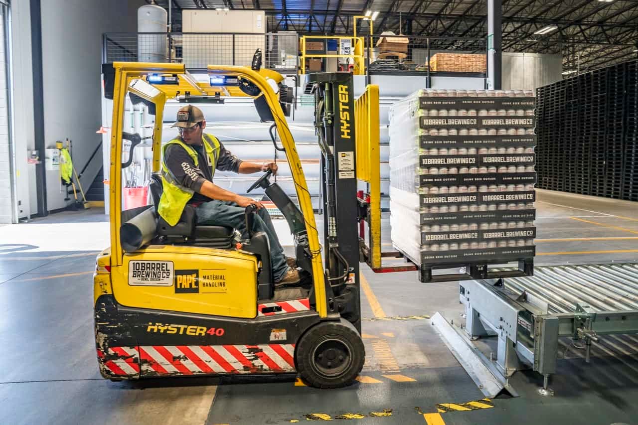 Forklift operator in yellow vest moving pallets of beer at warehouse facility