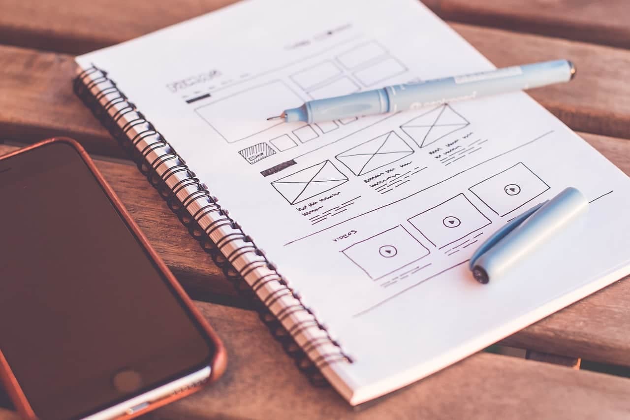 Website wireframe sketches drawn in spiral notebook with blue and gray pens and markers