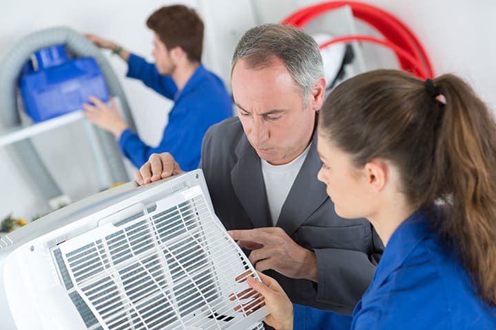 HVAC trainer and apprentice inspecting air conditioning unit in classroom