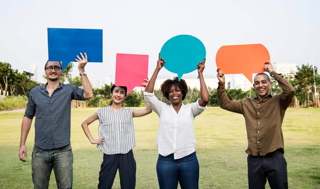 Four people holding colorful speech bubbles in outdoor field