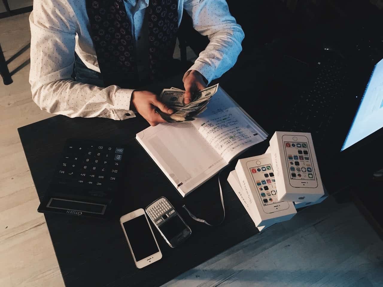 Overhead view of hands holding money and documents with calculator, notebook, and phones