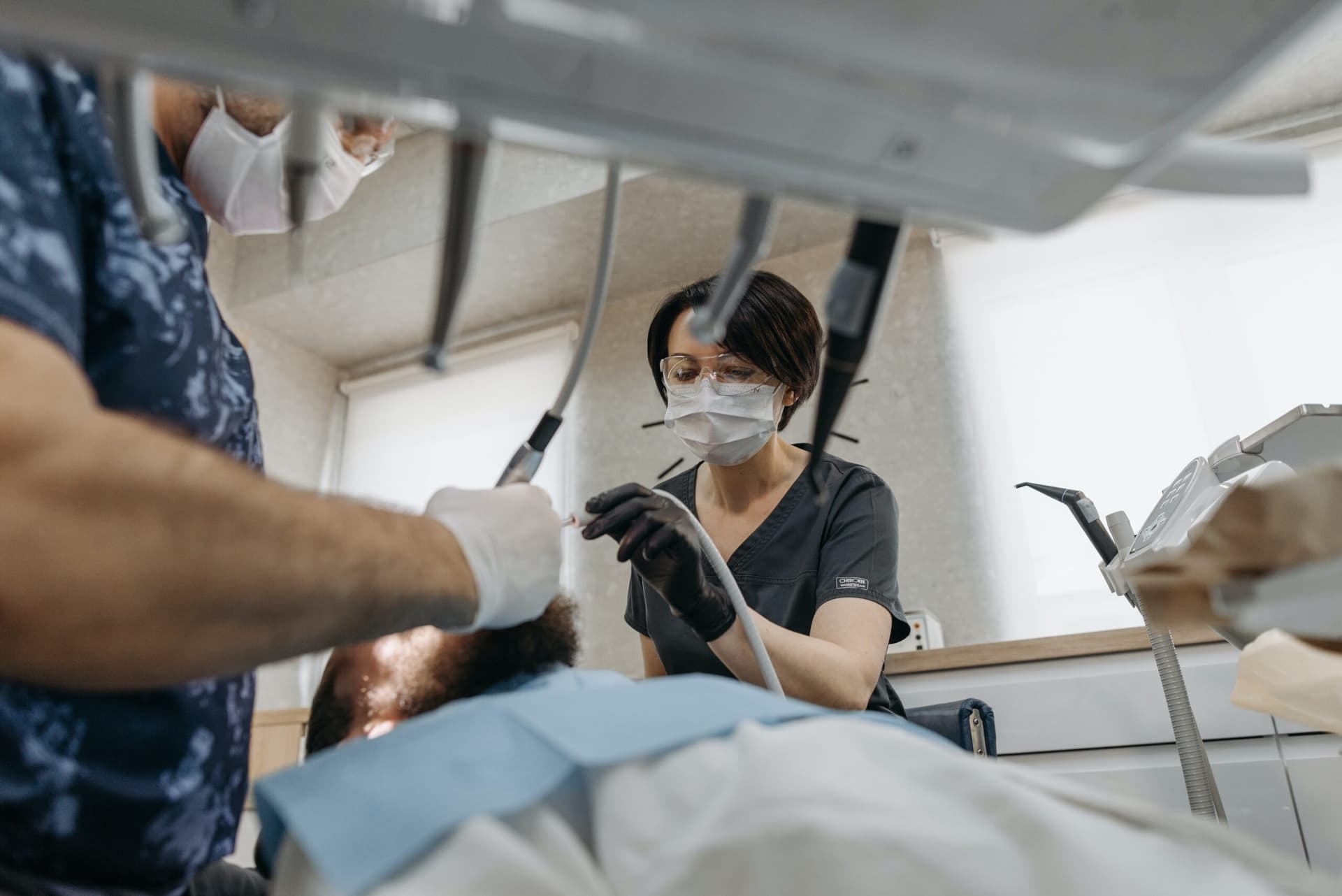 Dental professional in mask and gloves performing clinical procedure on patient in medical setting