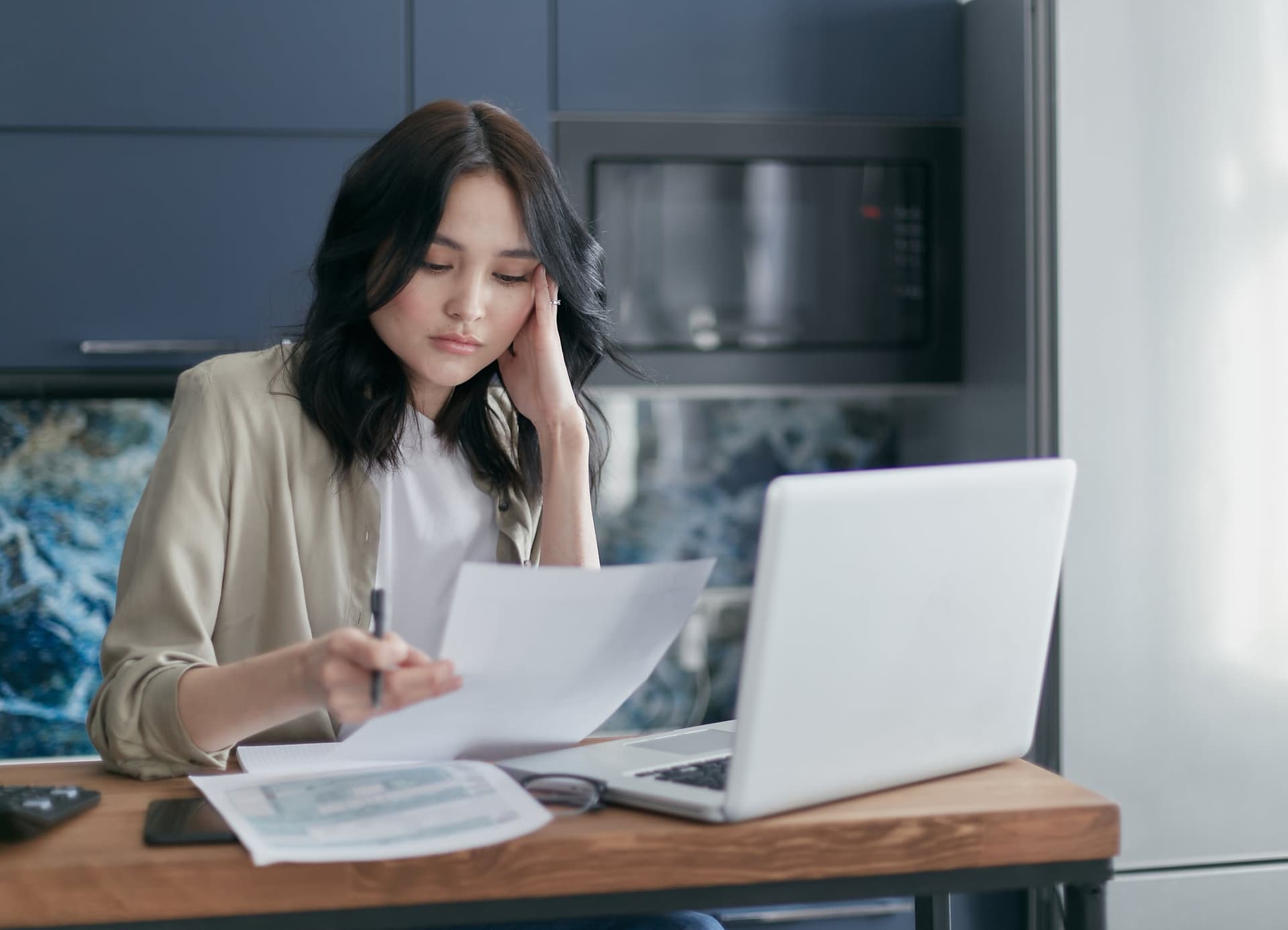 Woman at desk looking concerned while reviewing documents and laptop