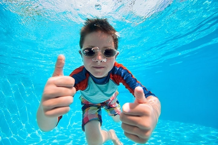 Child underwater in pool with goggles giving thumbs up signal