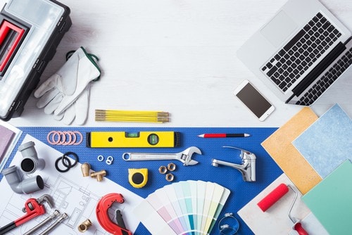 Overhead workspace with laptop, tools, paint color swatches, level, wrench, and construction equipment on blue surface