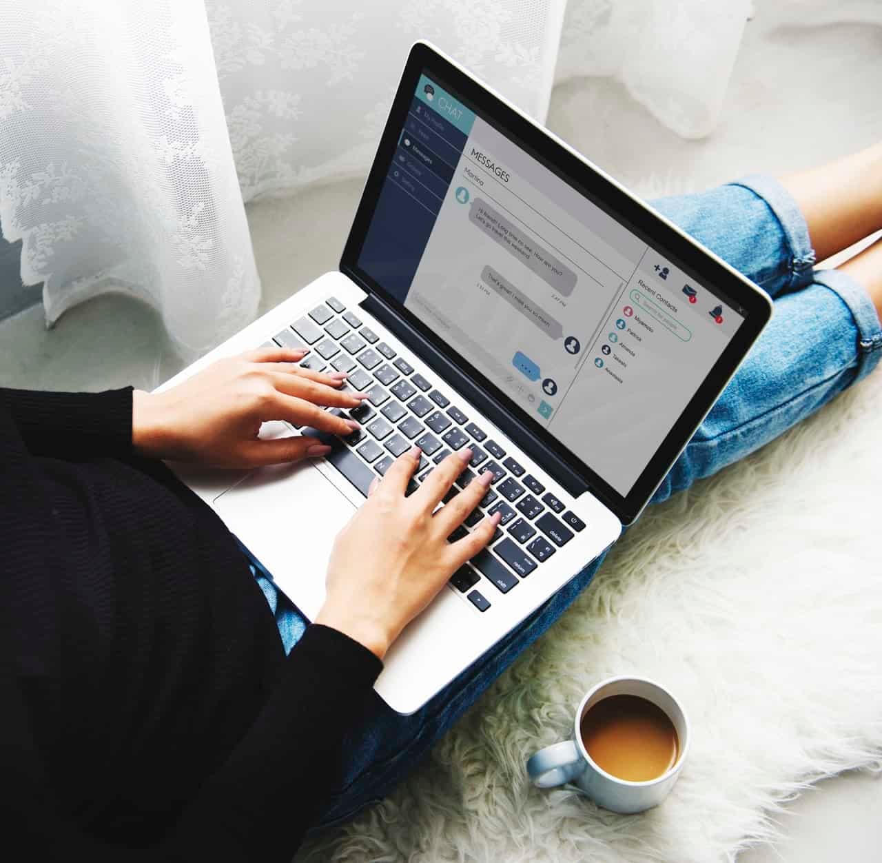 Hands typing on laptop with messaging interface on screen and coffee cup nearby