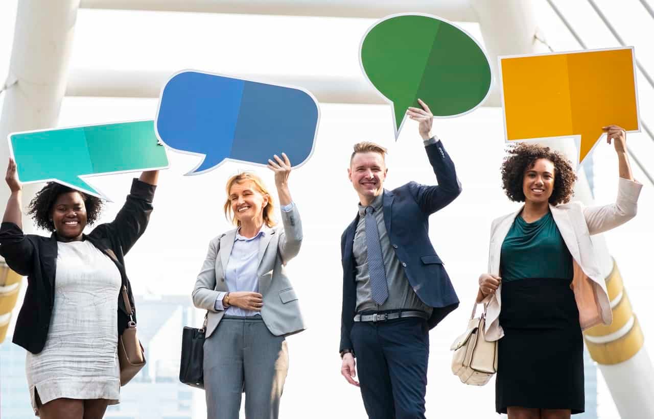 Four business professionals holding colored speech bubbles representing communication