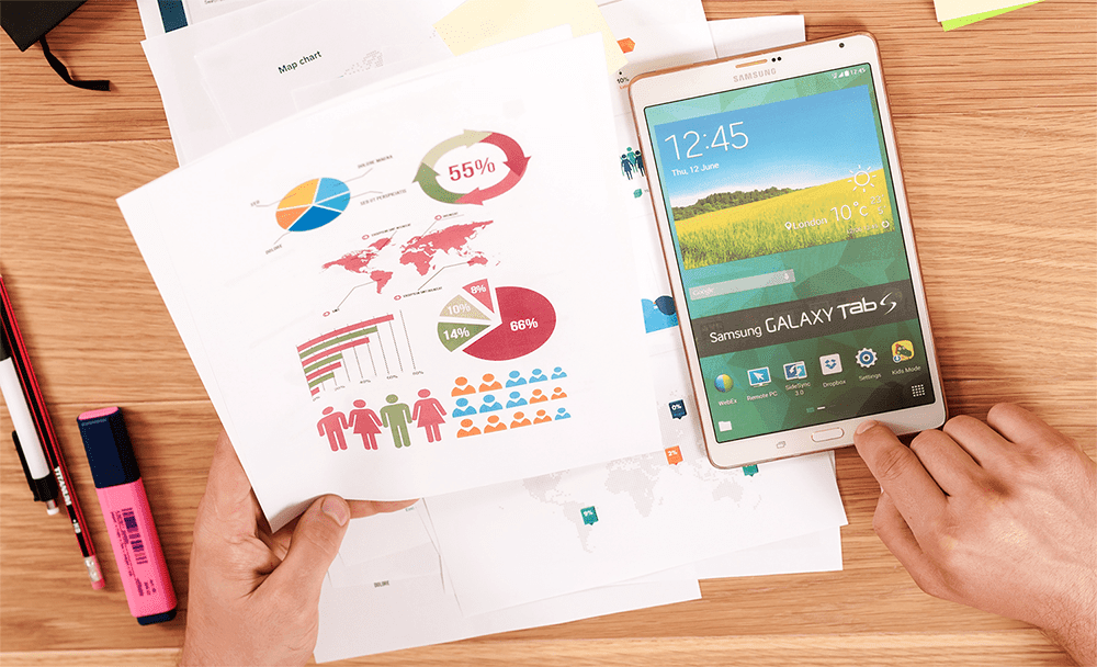 Hands holding analytics printout with colorful charts next to tablet