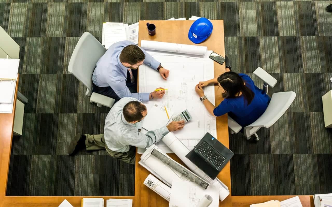 Overhead view of three professionals planning solar project at desk with blueprints