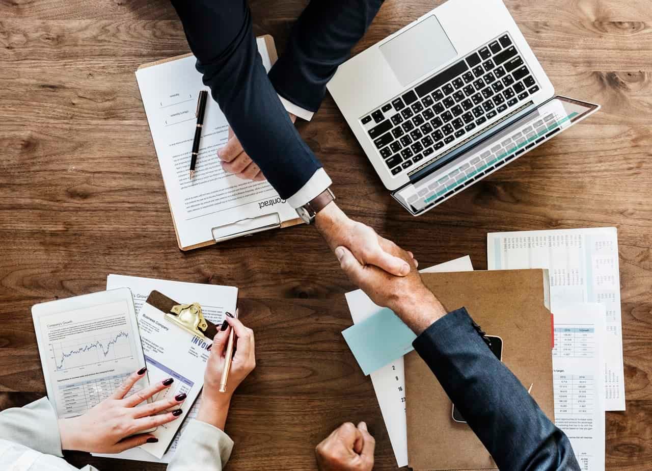 Overhead view of two people shaking hands over a desk with documents and a laptop