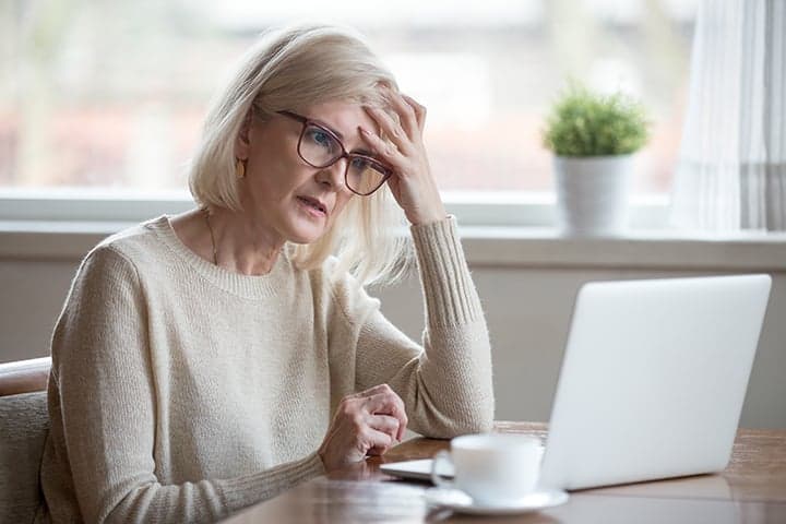 Woman in glasses at desk with laptop appearing concentrated
